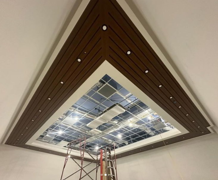 Triangular ceiling design with brown wooden panels, white trim, and recessed lights.