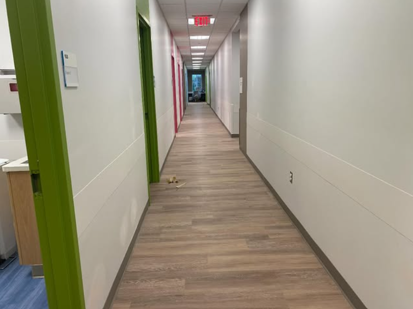 Long, brightly lit hospital hallway with colorful doors and wood-look flooring.