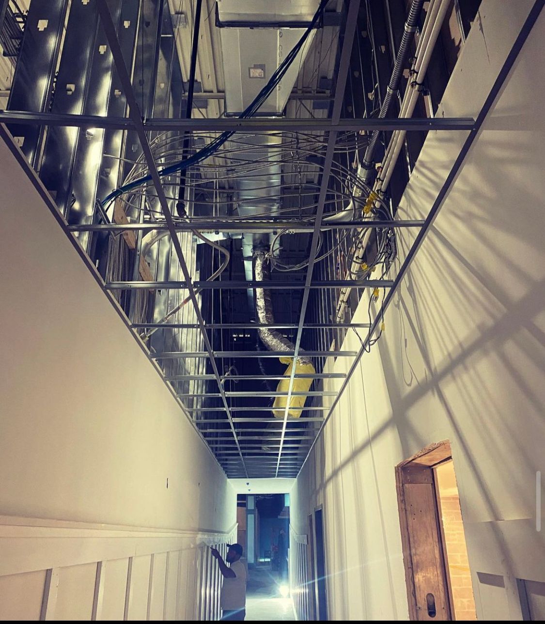 Hallway with exposed ceiling framework, electrical wiring, and a partially open doorway.