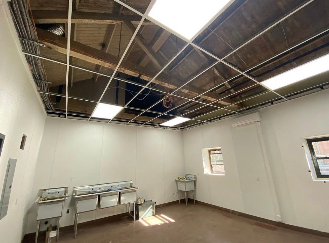 Interior view of a room under construction, with exposed ceiling beams, bright lights, and sinks along the wall.