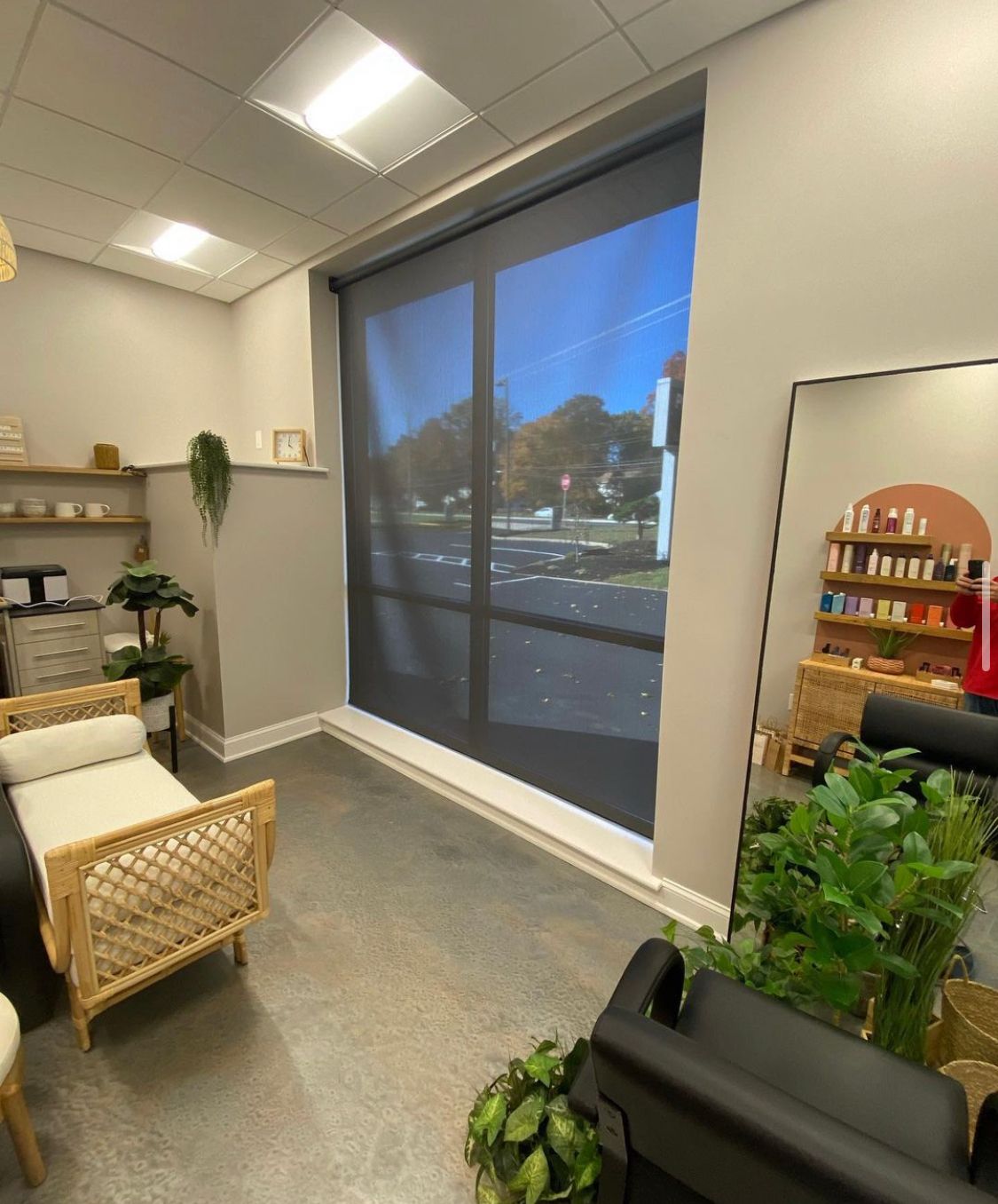 Interior of a room with a large window, a woven bench, a mirror, and shelves with products.