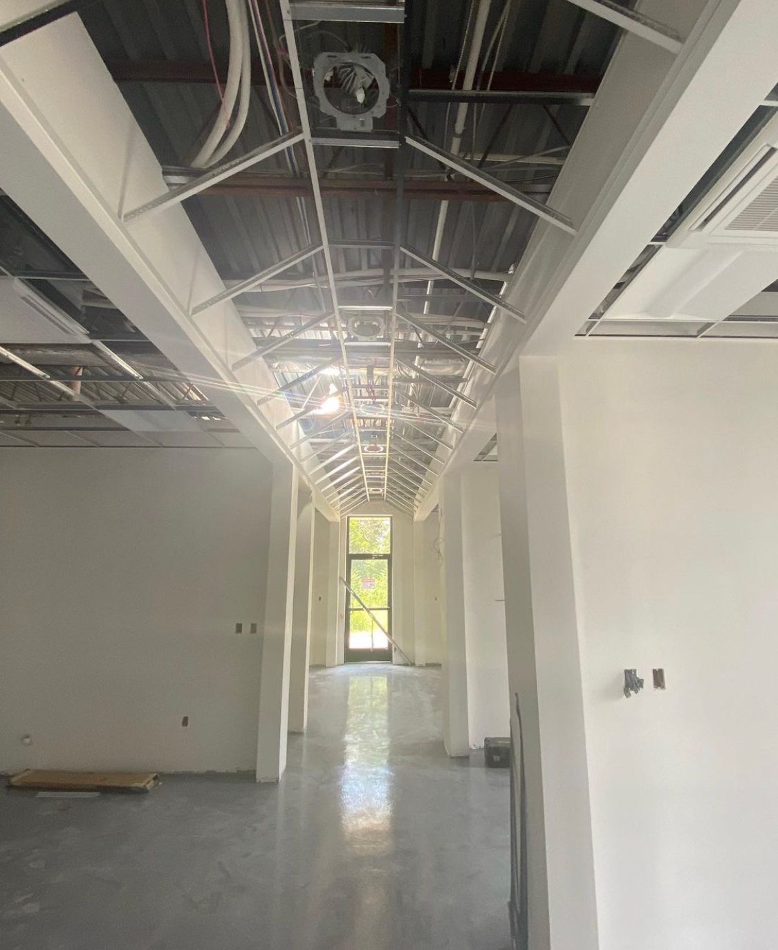 Exposed ceiling grid, white columns, and a bright doorway at the end.