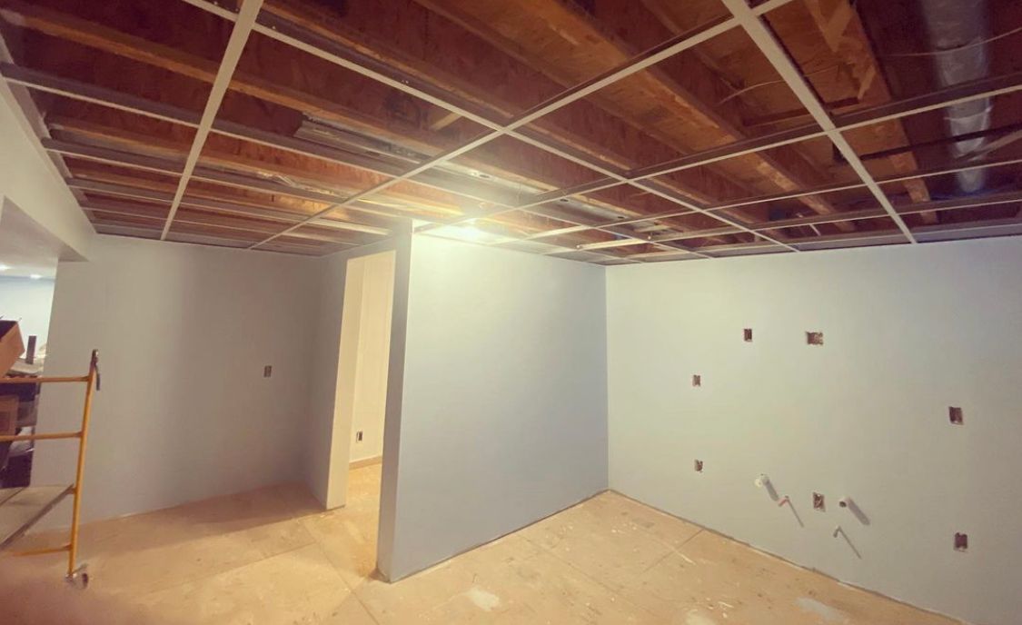 Interior room under construction with exposed ceiling beams and drywall.