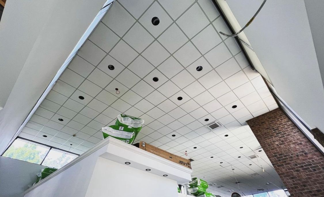 Ceiling with square tiles, recessed lights, and structural beams in a building interior.