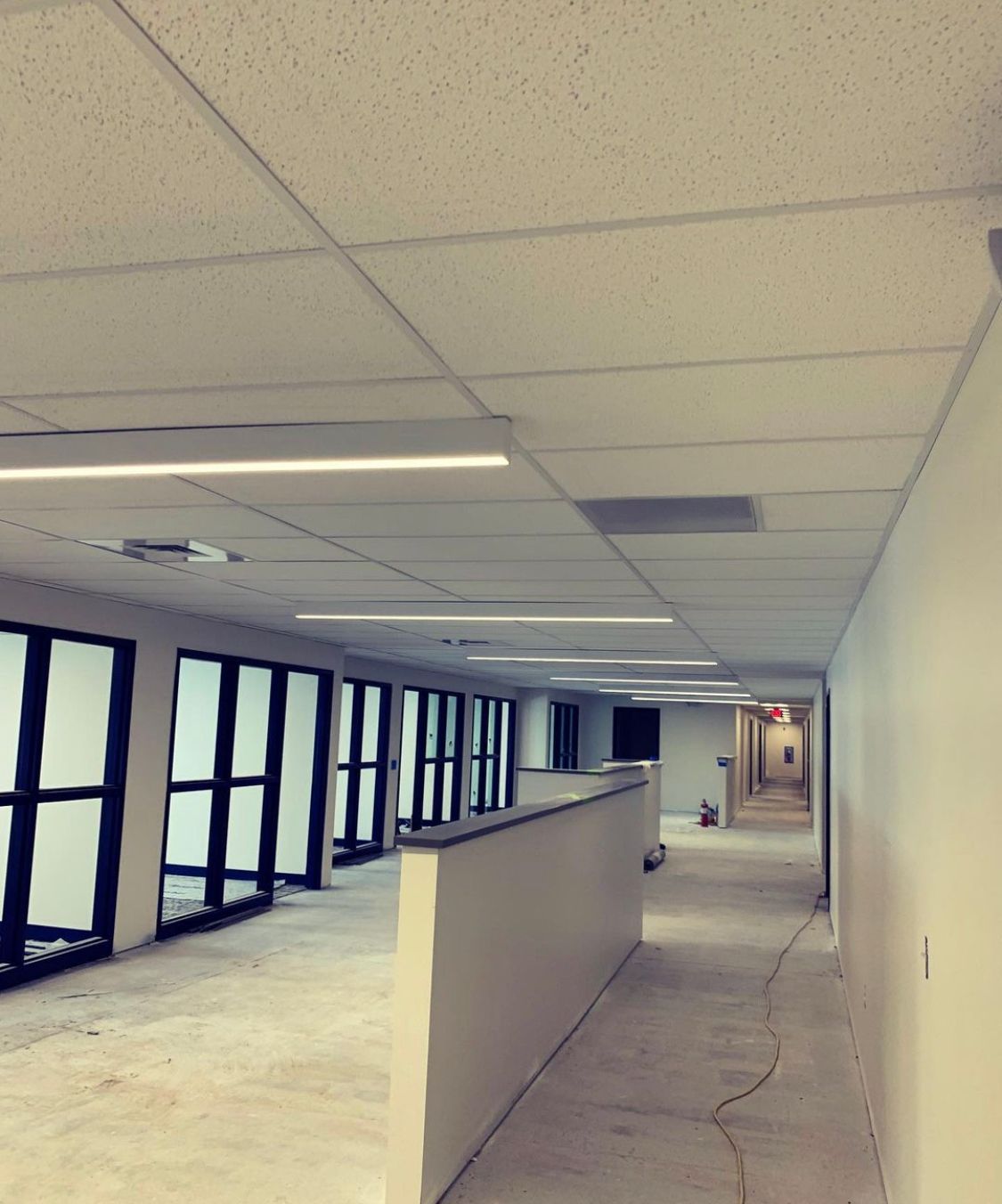Long office hallway with white walls and ceiling, glass windows and doors.