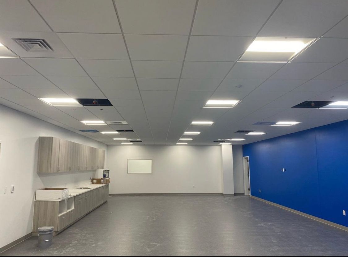 Empty office room with gray floor, white and blue walls, overhead lighting, and cabinets.