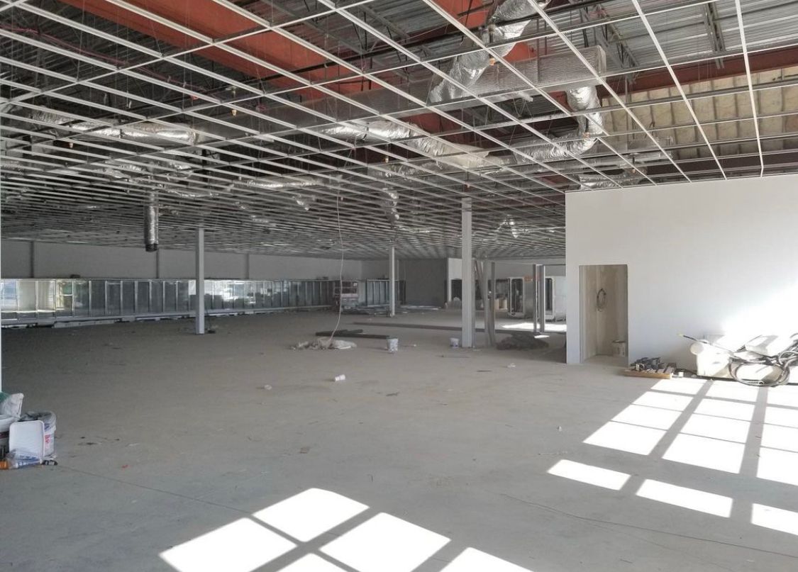 Interior of a large commercial space under construction with exposed ceiling supports and concrete floor.
