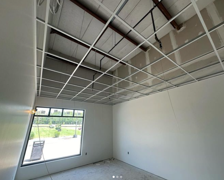 Room under construction: metal ceiling grid, drywall, window, and unfinished walls.