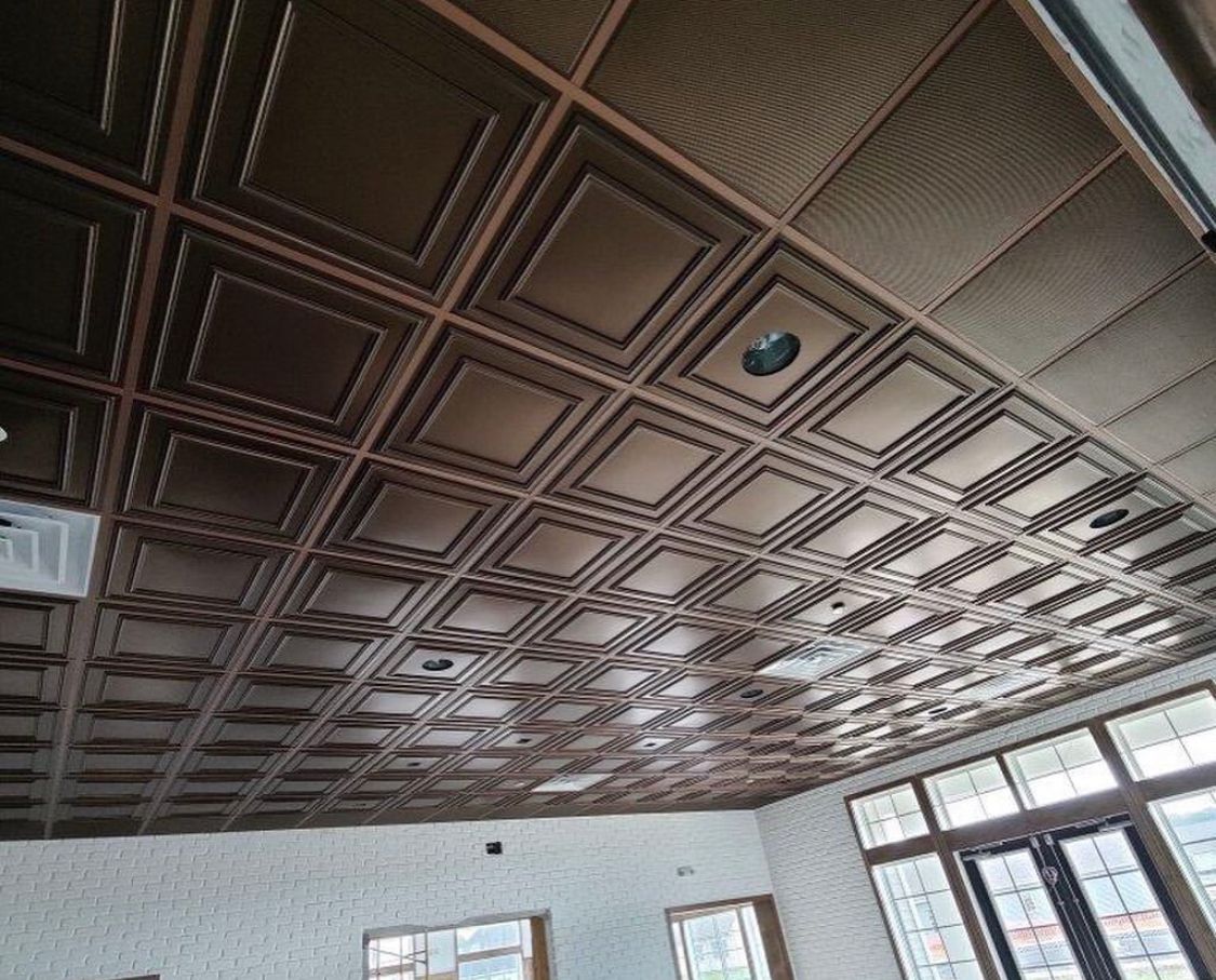 Brown patterned ceiling tiles in a room with a white wall and windows.