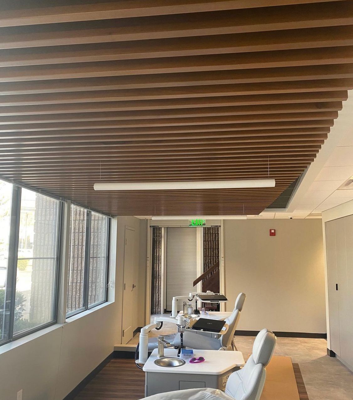 Dental office interior: wooden slat ceiling, dental chairs, windows, and a fluorescent light.