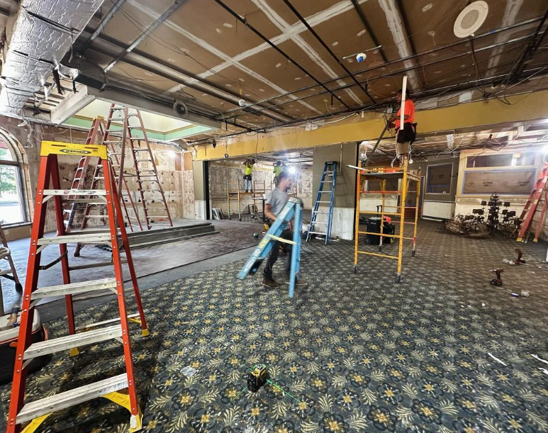Construction site with workers, ladders, exposed ceiling, and patterned carpet.