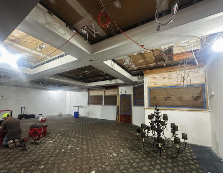Room under renovation; exposed ceiling beams, wiring, and partially torn-down walls. 