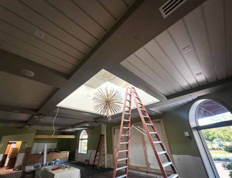Interior renovation with a chandelier, ladder, and a partially open ceiling. Green and gray walls.