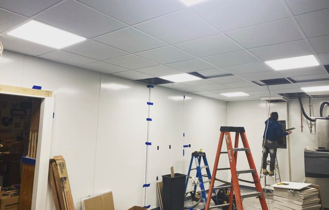 Construction in a room with white walls and ceiling. A worker on a ladder. Electrical work in progress.