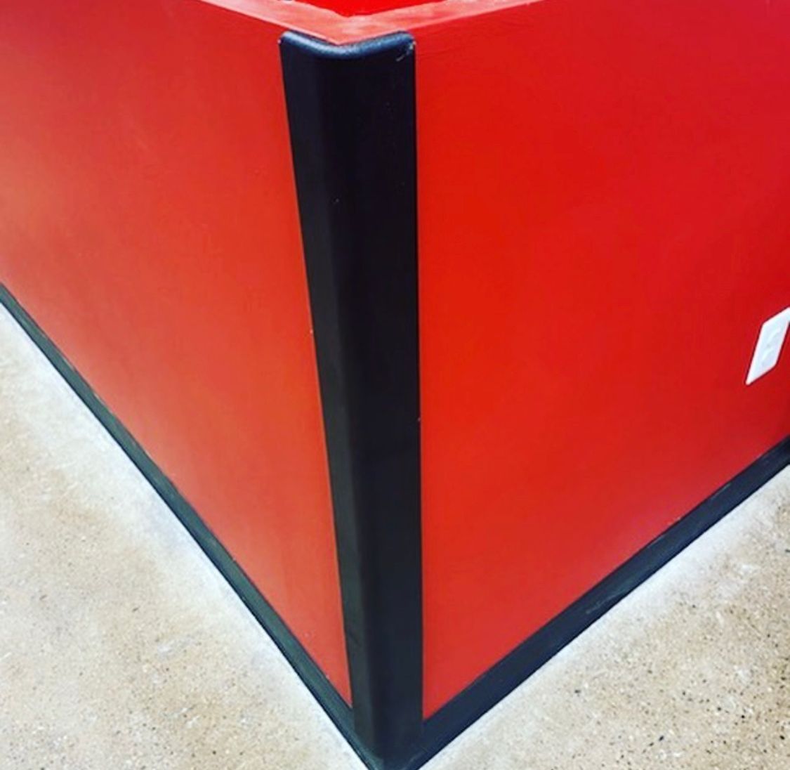 Red box corner with black corner guards on a concrete floor.