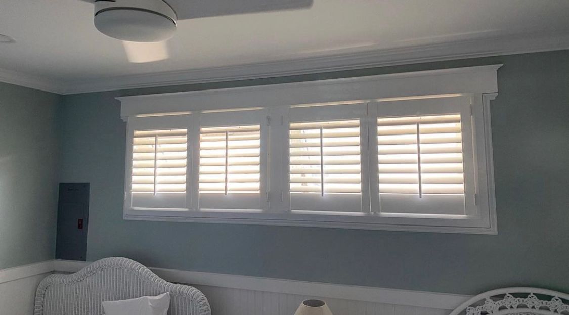 Bedroom with white window shutters and trim, soft blue walls.