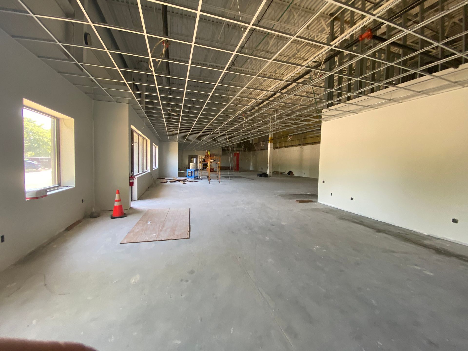 Interior of a building under construction, showing bare walls, open ceiling grid, and concrete floor.