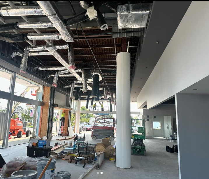 Interior under construction, showing exposed ceiling with ductwork and a cylindrical support column.