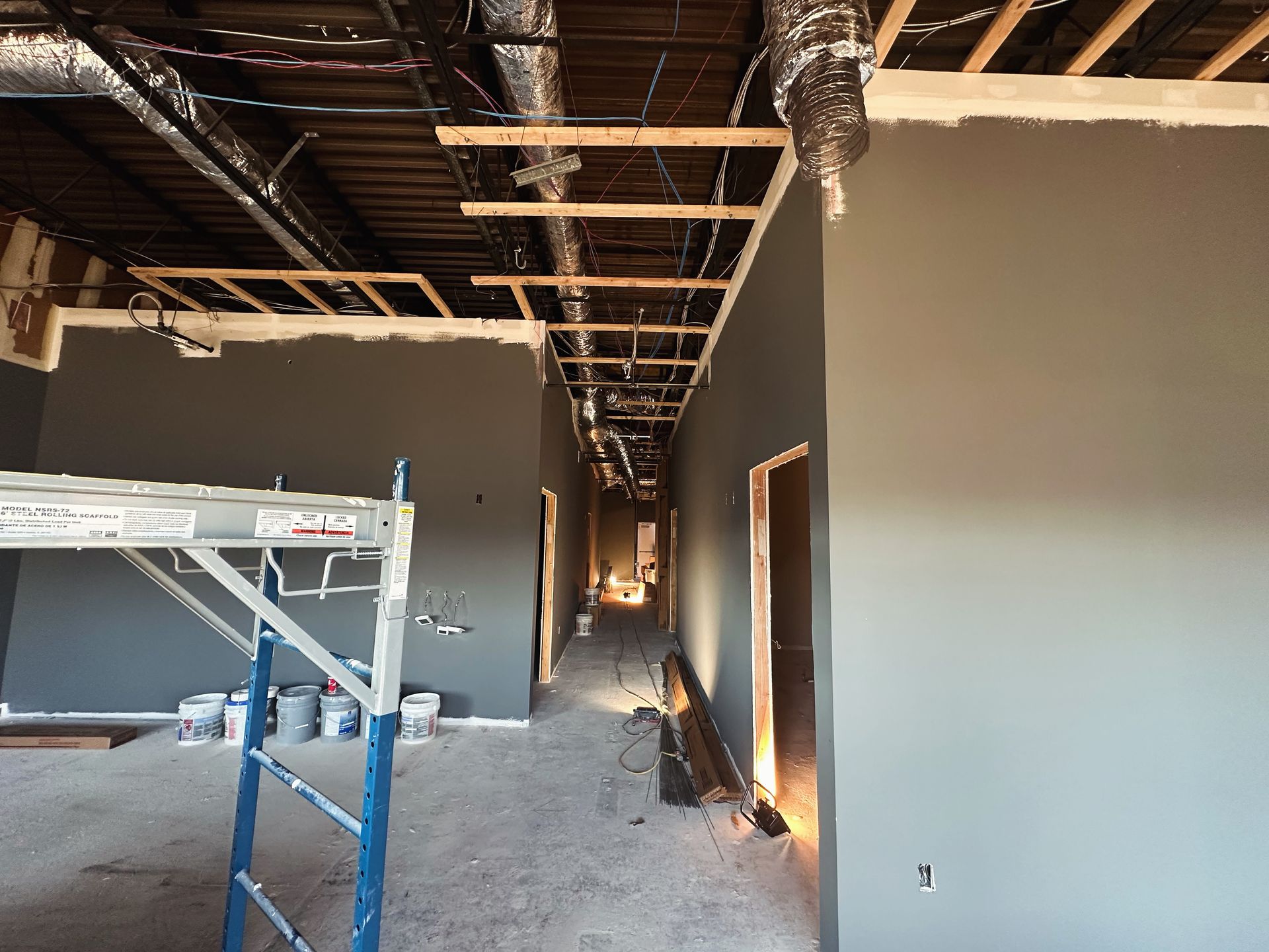 Interior of a building under construction, with gray walls, exposed ceiling beams, and a scaffold.