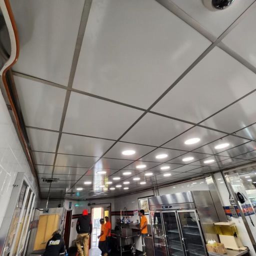 Restaurant kitchen ceiling with metal grid and recessed lights; workers in the room.