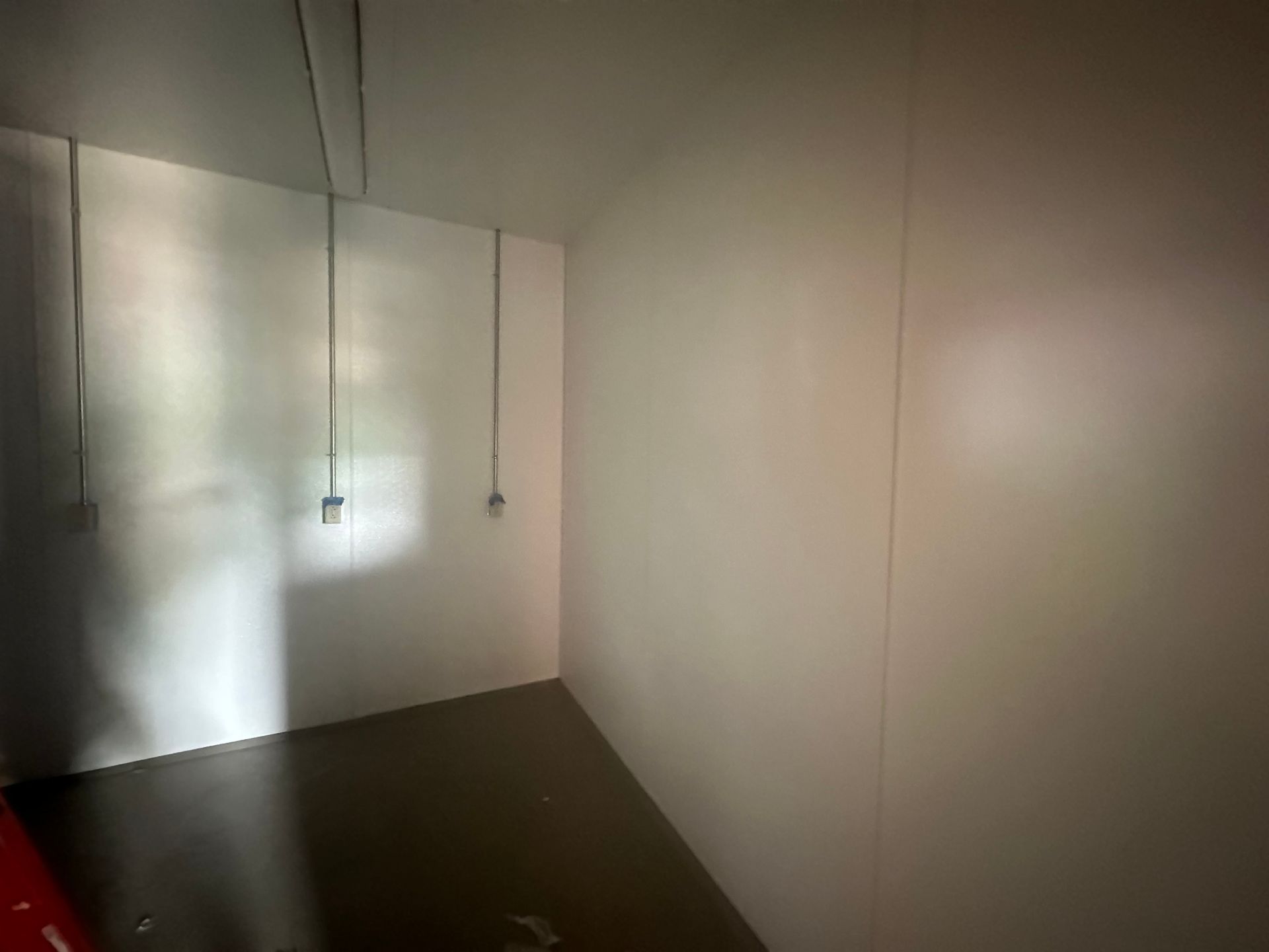 Empty storage room with white walls, dark floor, and electrical outlets.
