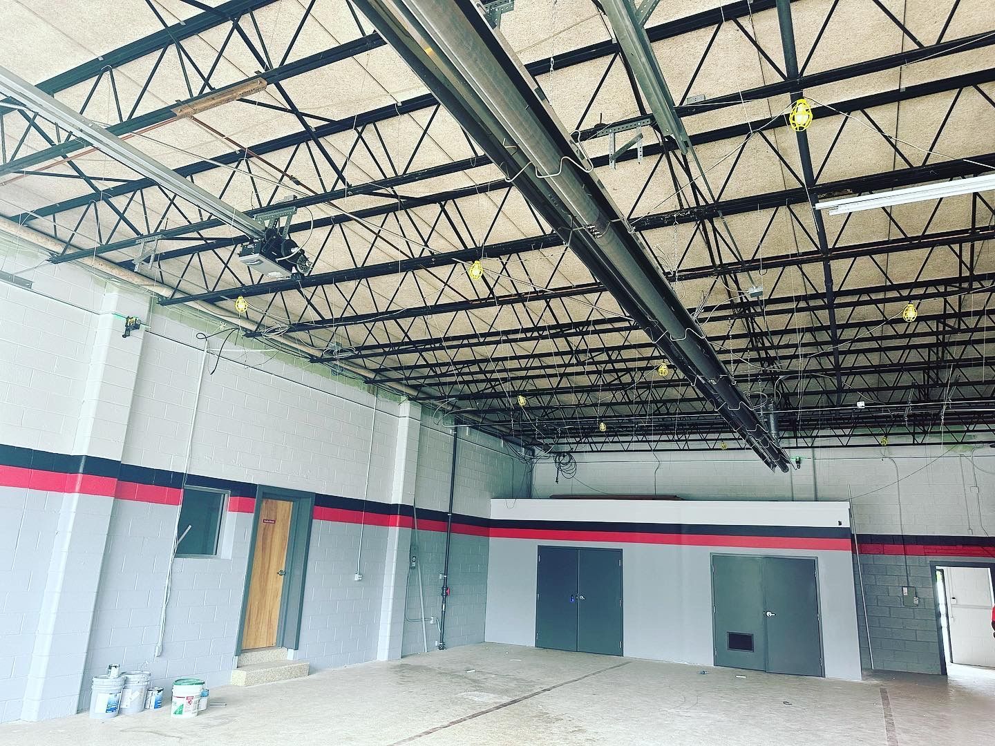 Interior of a commercial space, gray walls with red stripes, exposed ceiling trusses, and several closed doors.