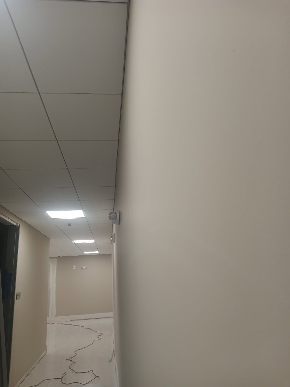 Hallway with white walls, drop ceiling, and recessed lights. Beige-colored flooring.