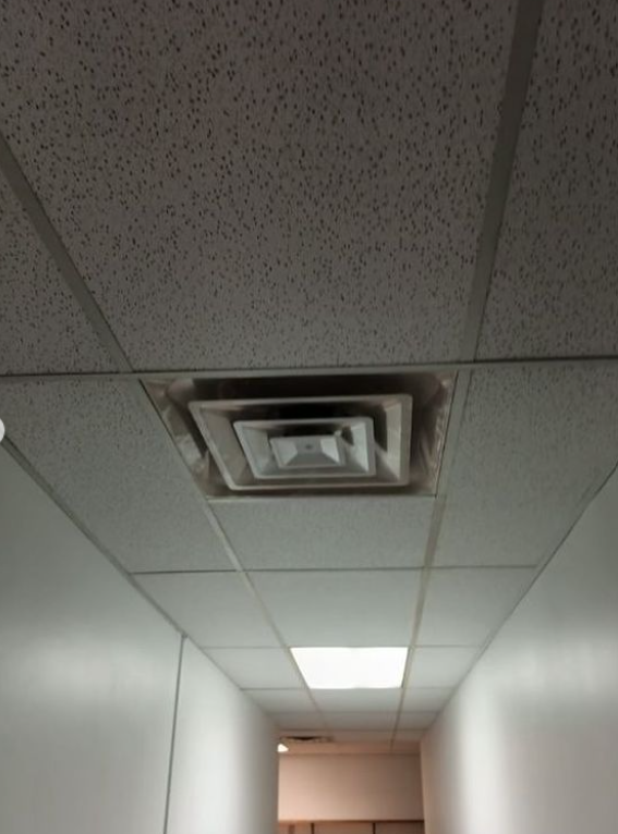 A ceiling with a ventilation vent and fluorescent lighting in a hallway.