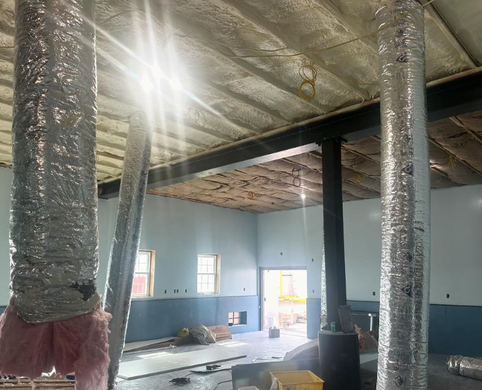 Interior construction view: ductwork, exposed beams, insulation on ceiling, natural light streaming through a doorway.