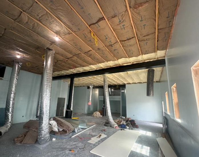Interior room under construction with exposed beams, insulation, ductwork, and debris.