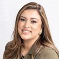 Tati smiling, wearing a green blazer, against a white backdrop.