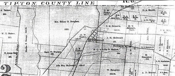 The brick exterior of Kerrville, a rustic building with a wooden porch and centered wooden door, under a clear sky.