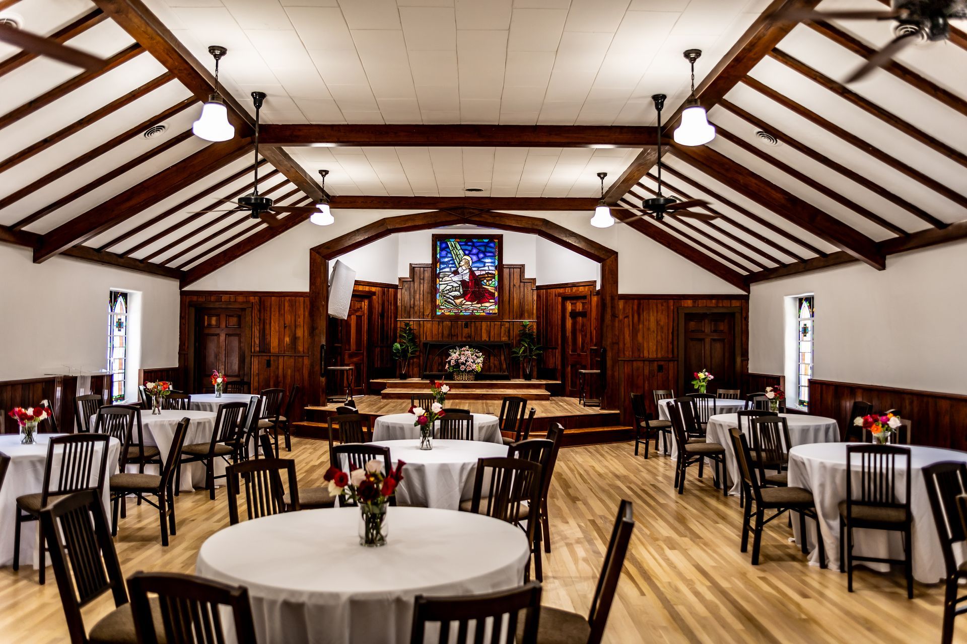 A minimalist indoor chapel with a central wooden altar, rows of chairs, and a green runner on a light wood floor.