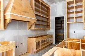Unfinished kitchen renovation: wooden cabinets, range hood, and pantry in a room with drywall.
