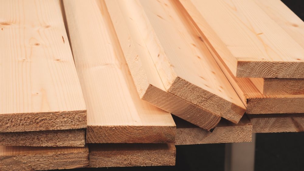 Stack of light-colored wooden planks with visible grain and rough-cut edges.