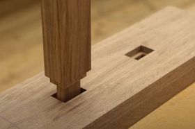 Close-up of a wooden mortise and tenon joint partially assembled. Brown wood with visible grain.