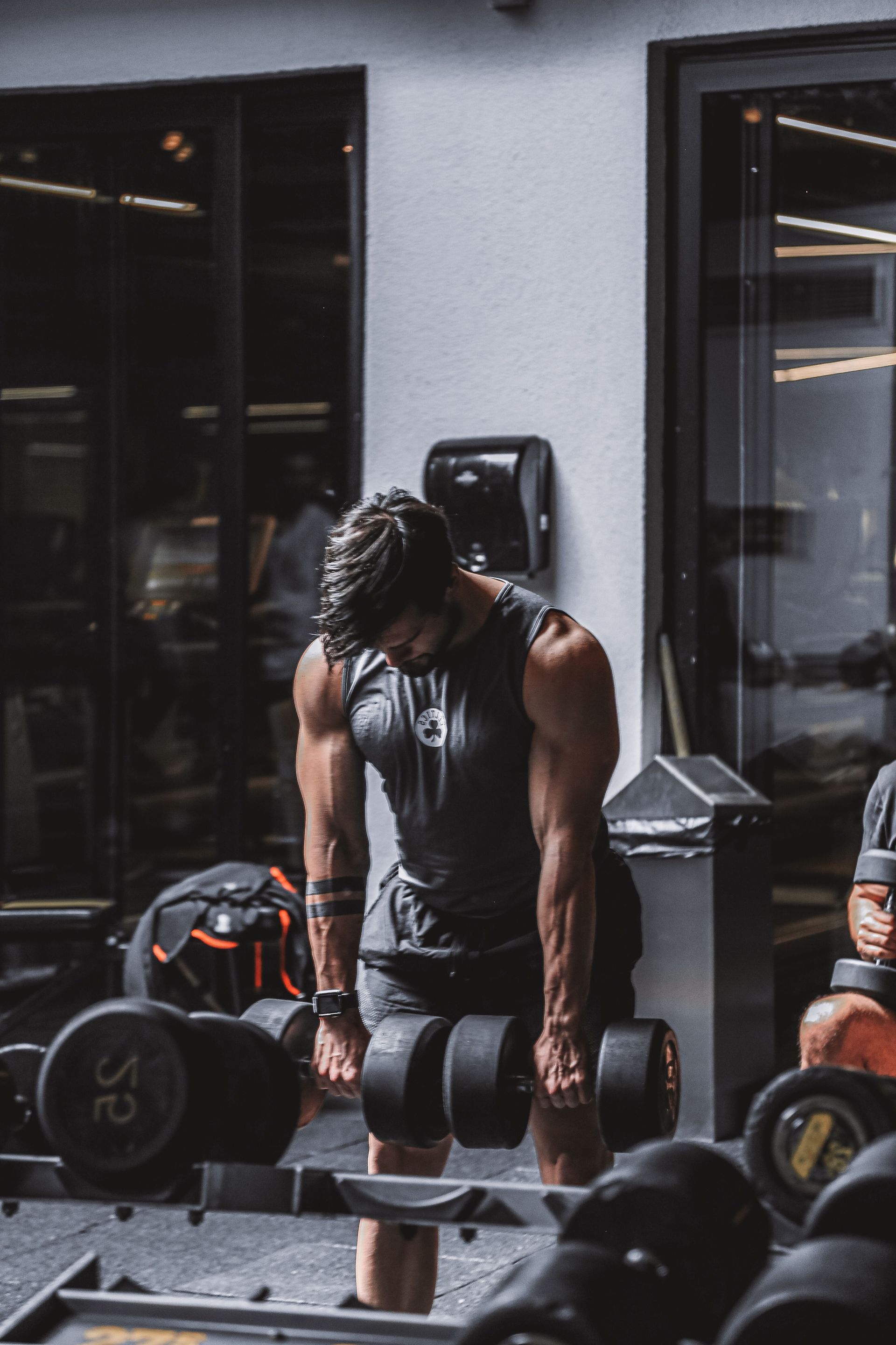 Person lifting dumbbells in a gym, wearing a black tank top and shorts.