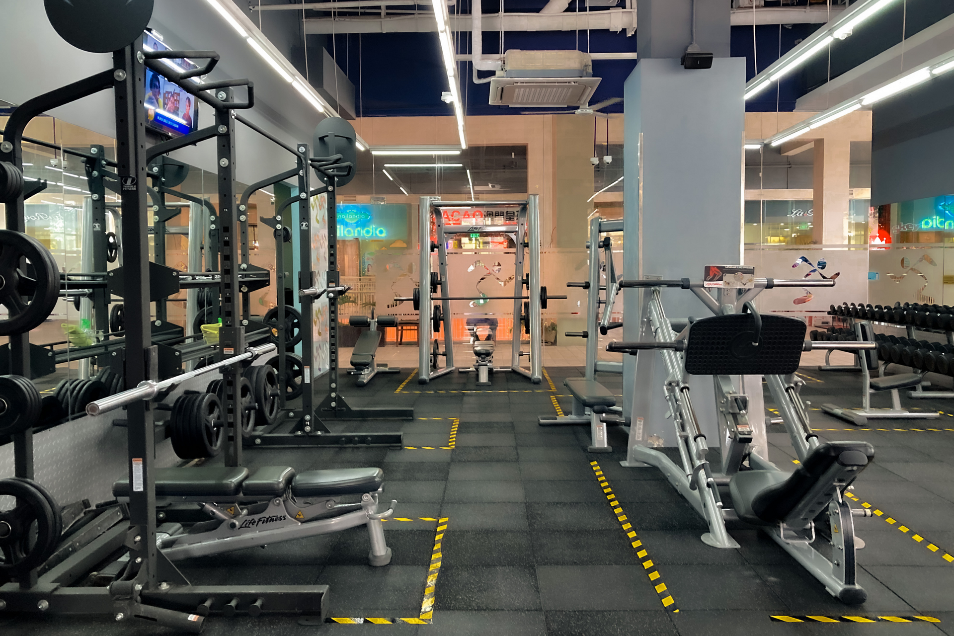 Modern gym with weight machines, treadmills, and a central turf walkway under bright overhead lights