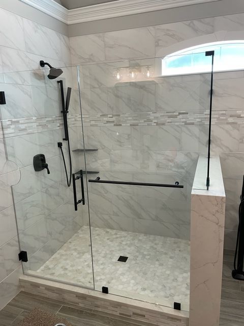 Modern glass shower enclosure with black hardware, white tile walls, and stone floor.