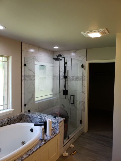 Bathroom with a white tub, granite countertop, and a glass shower with black fixtures and tile.