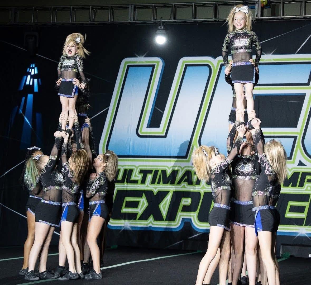 Cheerleaders in black and blue outfits performing a stunt on a stage with “Ultimate Expo” backdrop