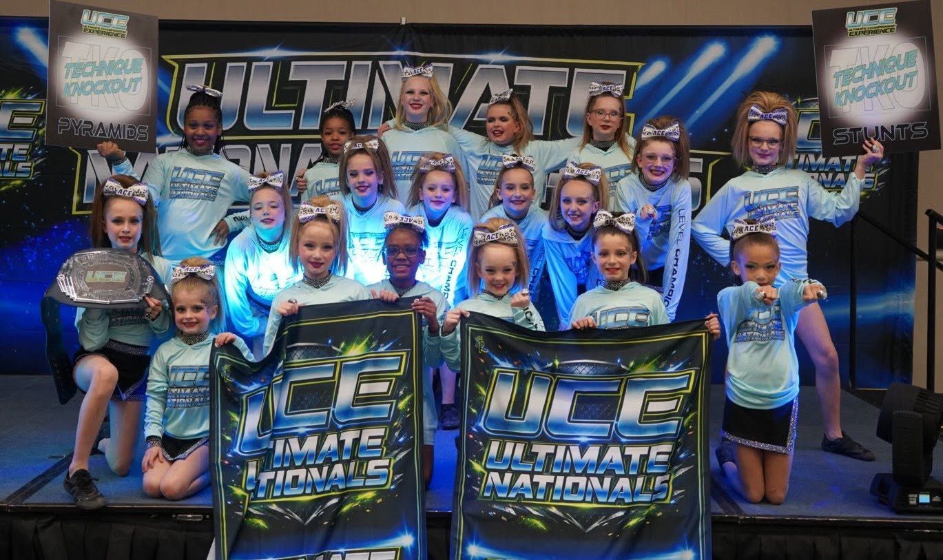 Cheerleading team posing on stage with trophies and a large “Ultimate” competition banner behind them