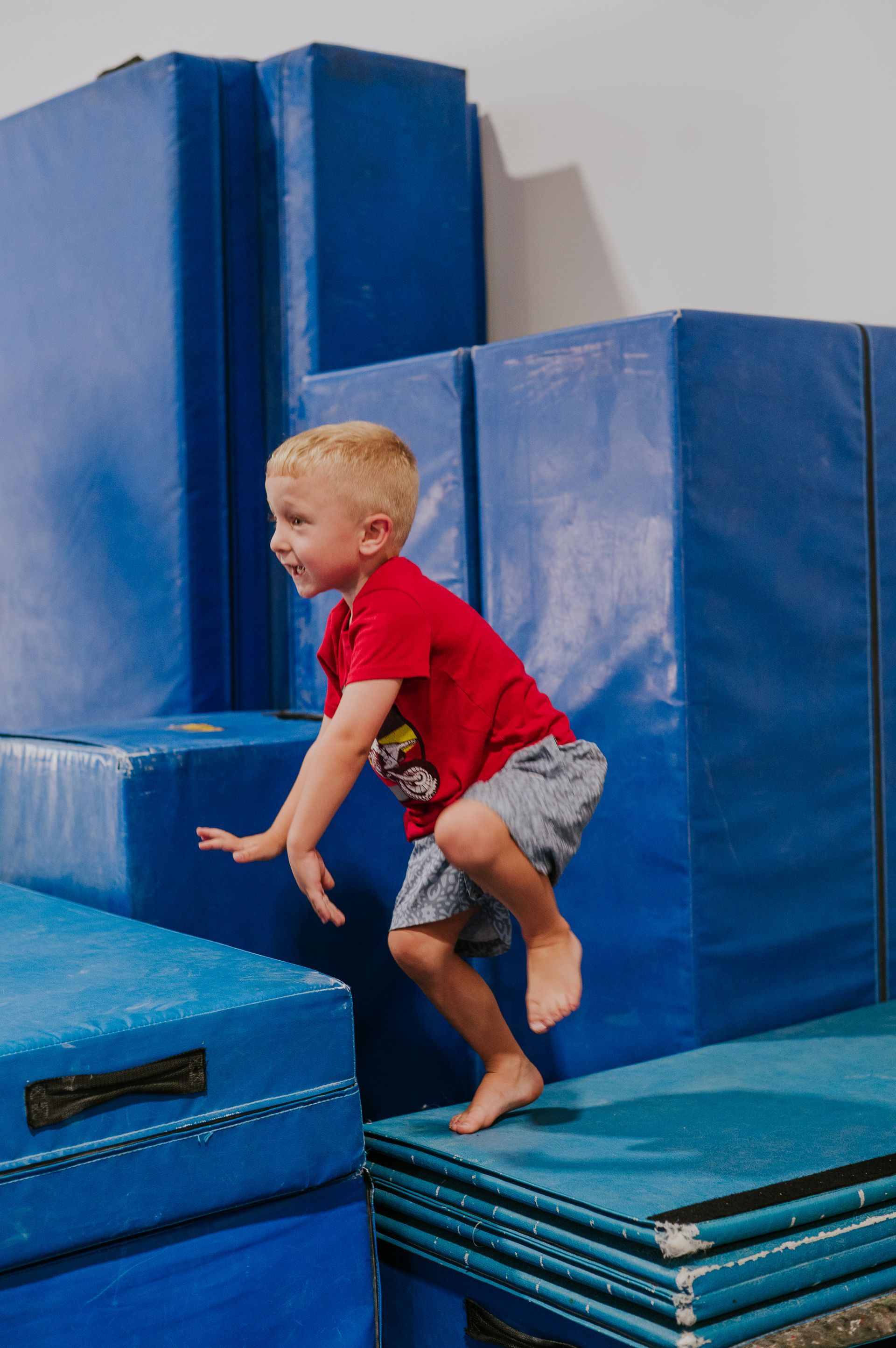 Child climbing on blue padded gym blocks indoors