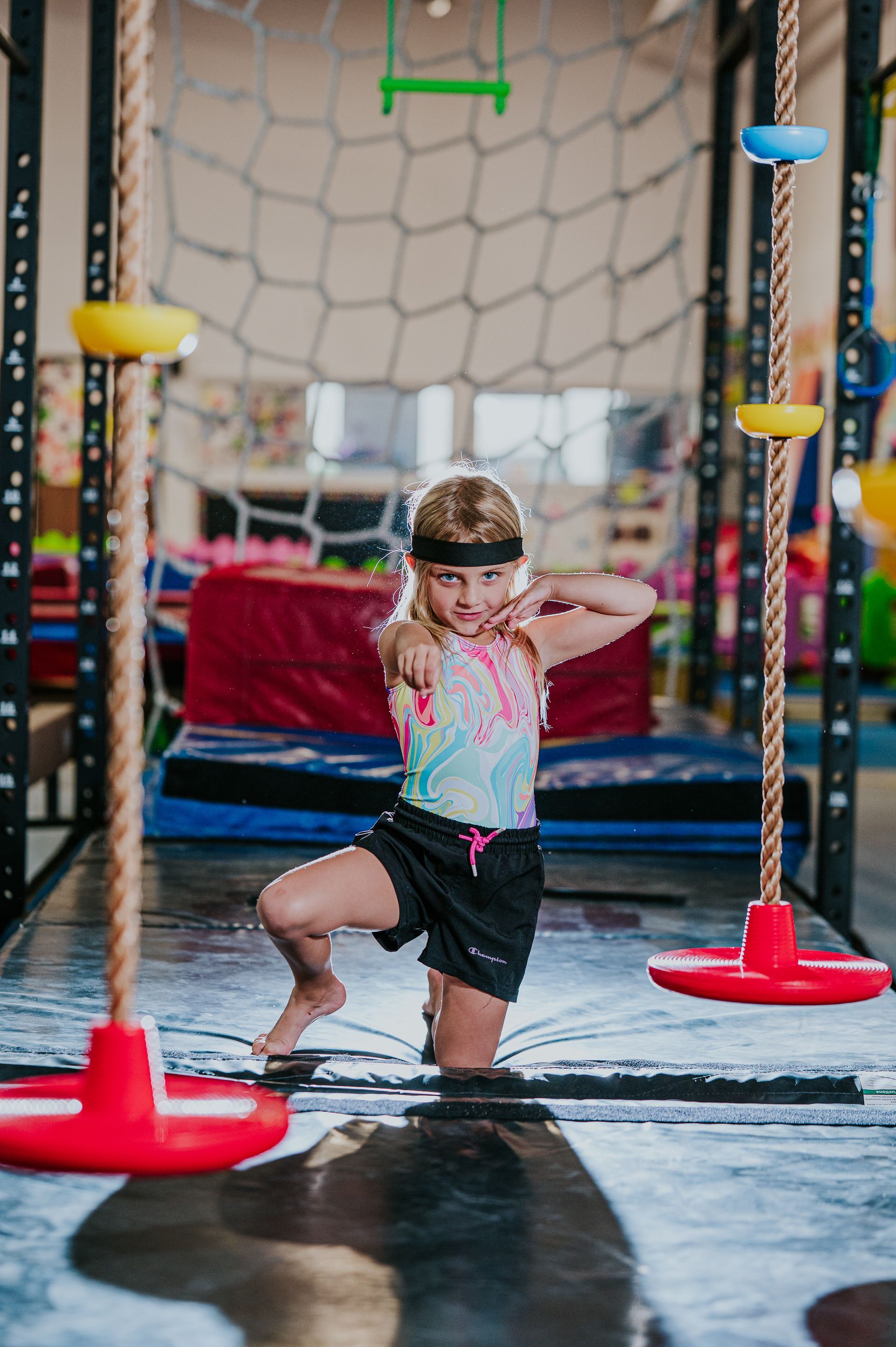 Child balancing on a play obstacle course with red and yellow equipment in an indoor gym