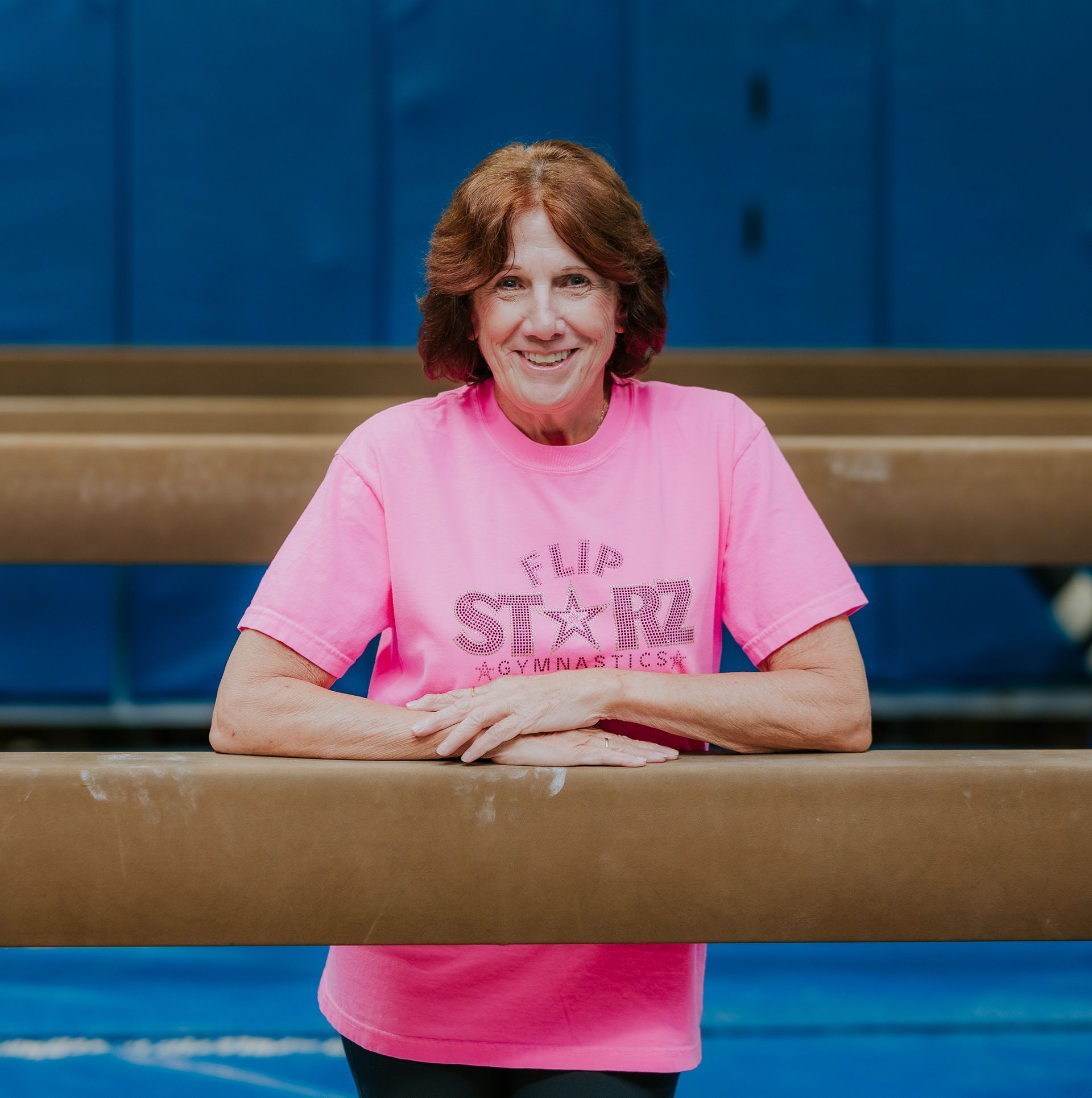 Person in a pink shirt leaning on a wooden railing in a blue indoor setting.