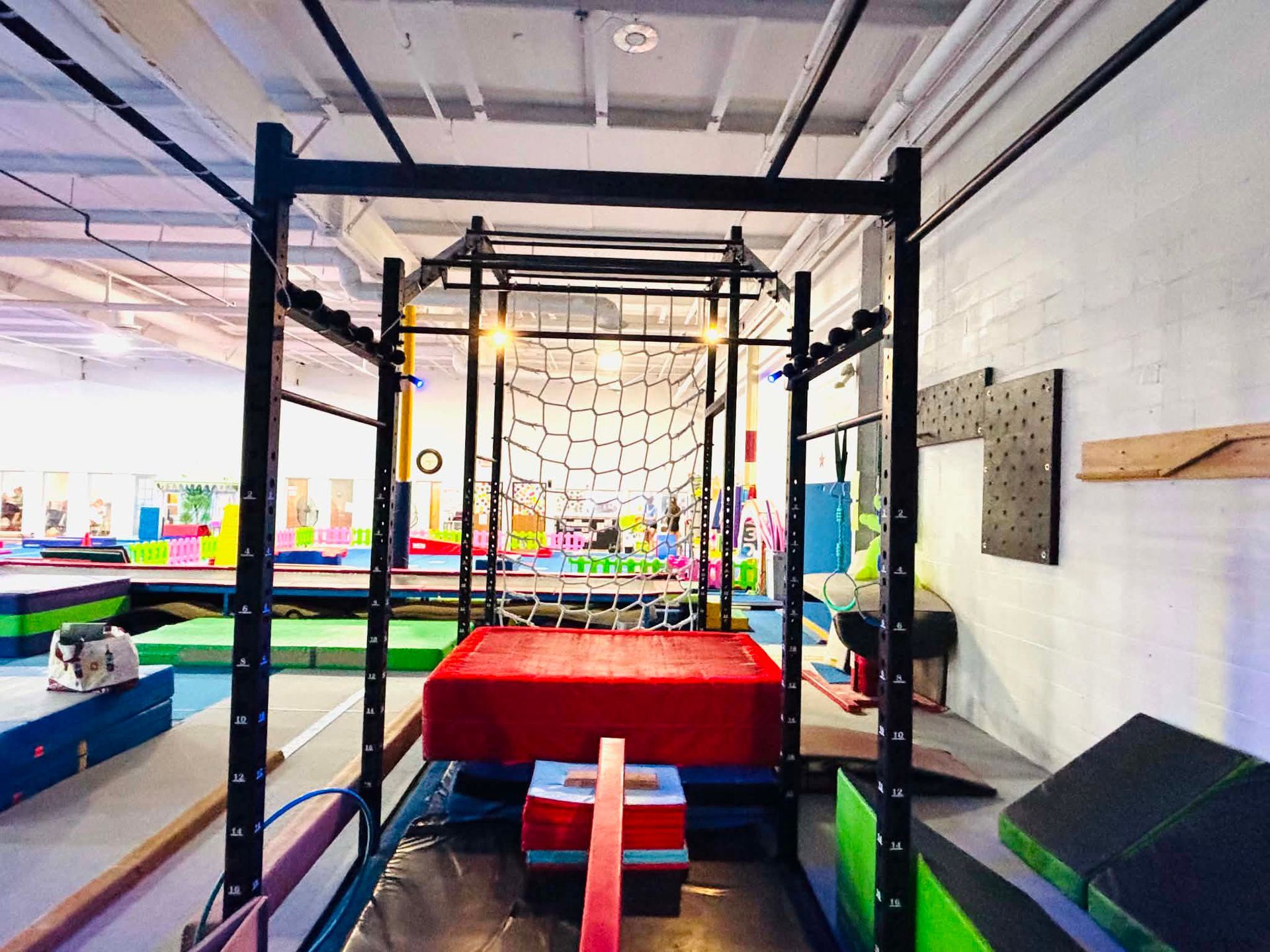 Indoor ninja obstacle course with hanging rings, ropes, and a red padded platform in a gym