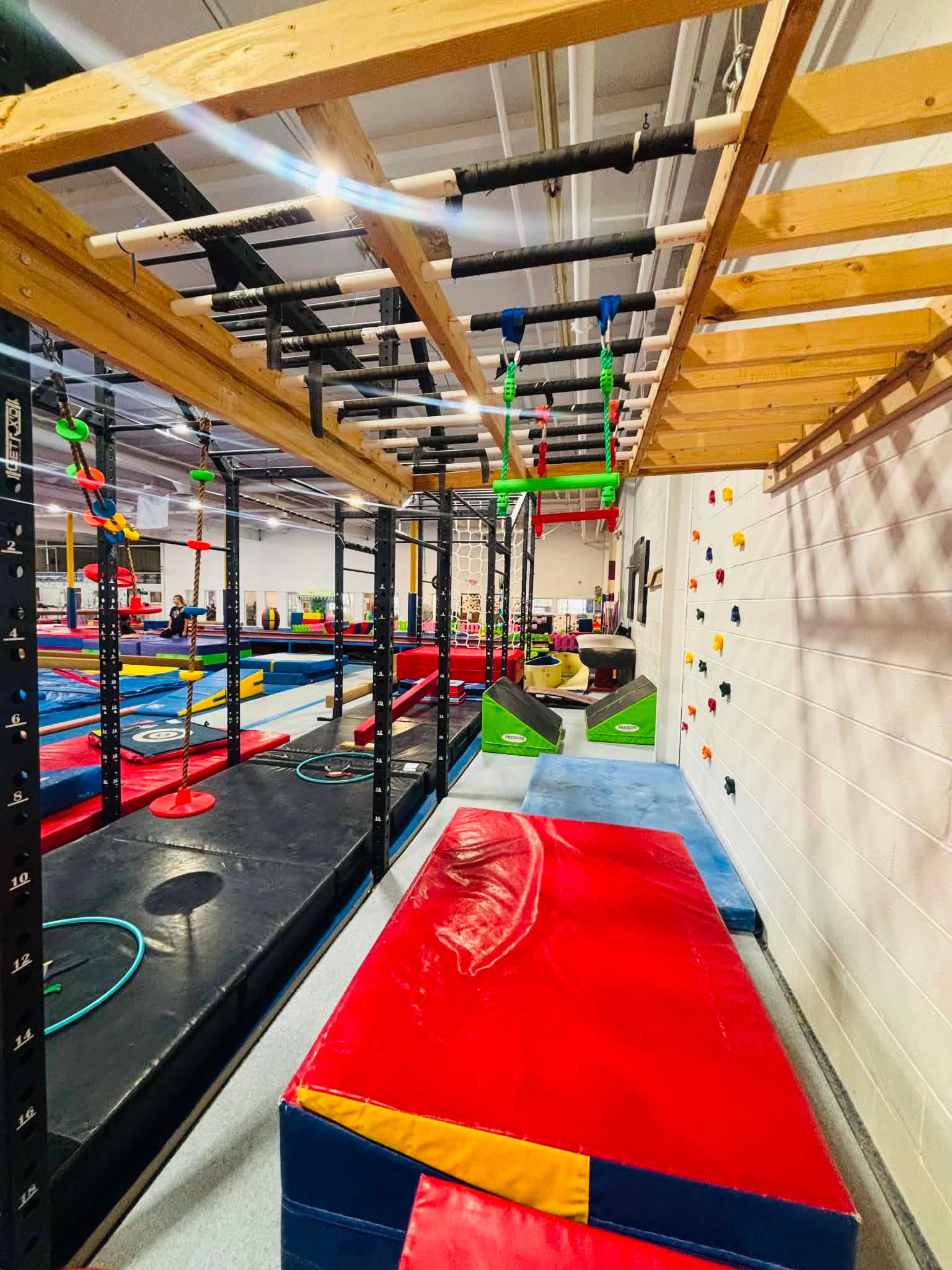 Indoor obstacle course with colorful padded platforms, ropes, and climbing structures under bright ceiling lights