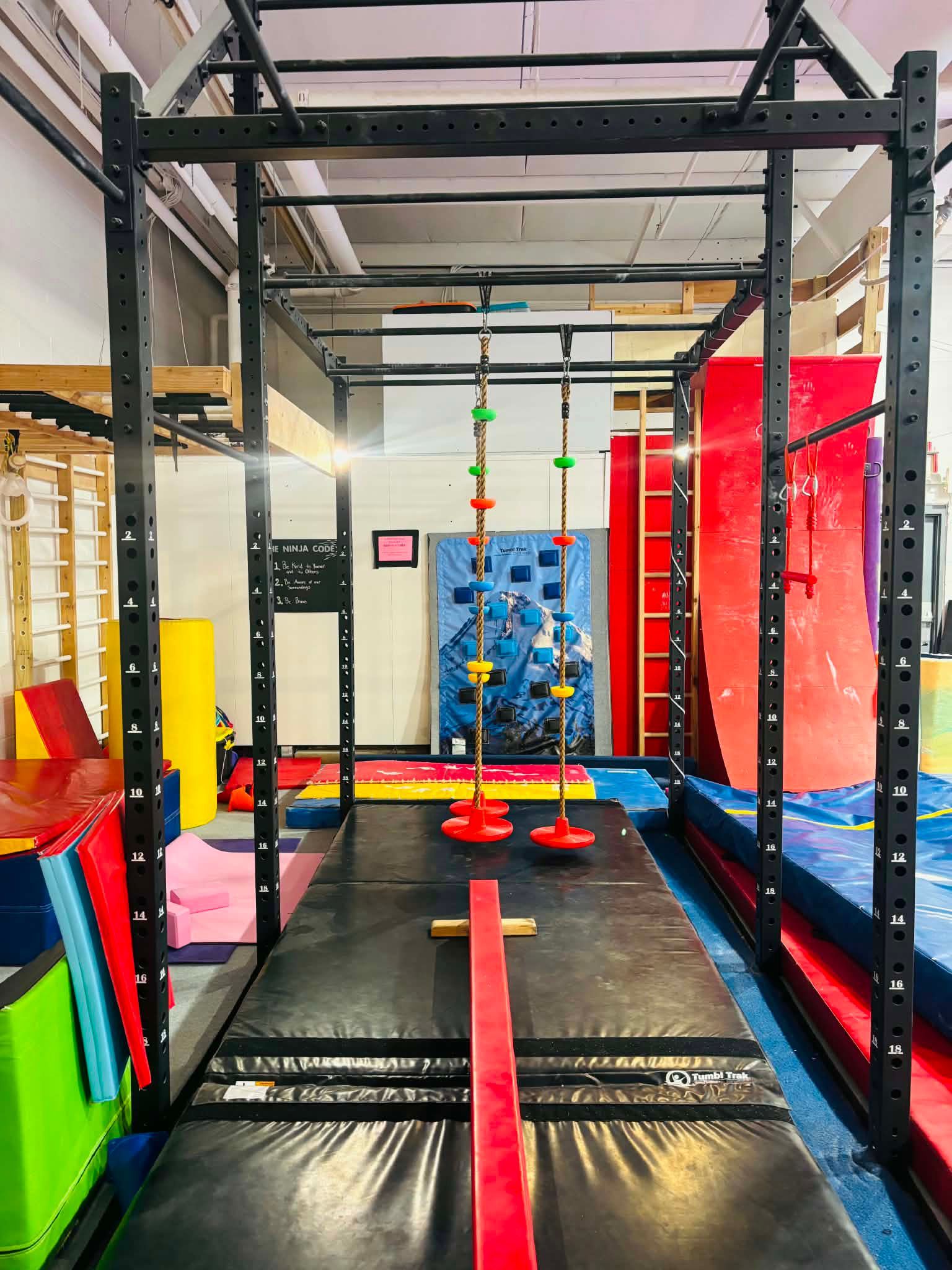 Indoor obstacle course with black metal frames, hanging grips, mats, and colorful climbing holds