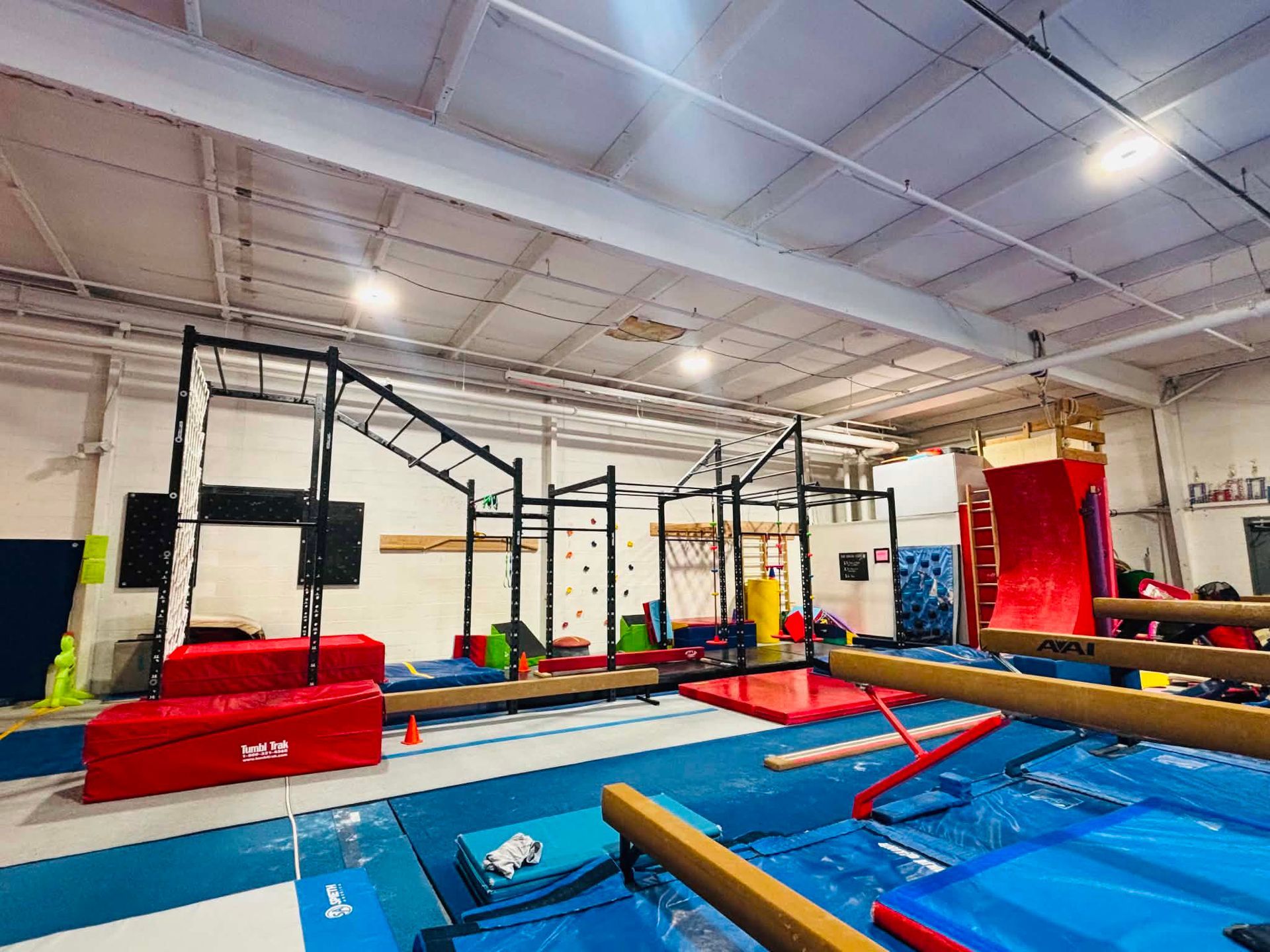 Indoor gymnastics obstacle course with blue mats, red padded blocks, and metal climbing frames