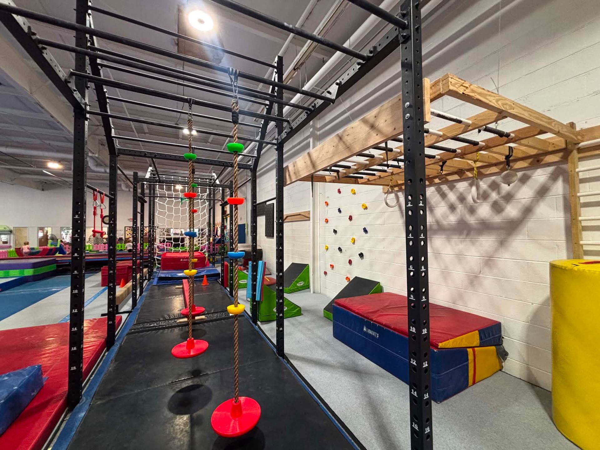 Indoor obstacle course with hanging red discs, mats, and climbing frames in a gym-like play space